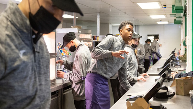 Food service team working behind a counter in a busy cafeteria.