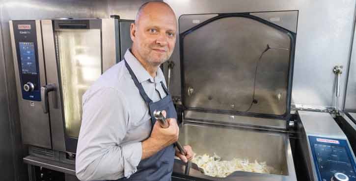Simon Rogan smiles at the camera whilst he stirs onions in the iVario Pro L model.