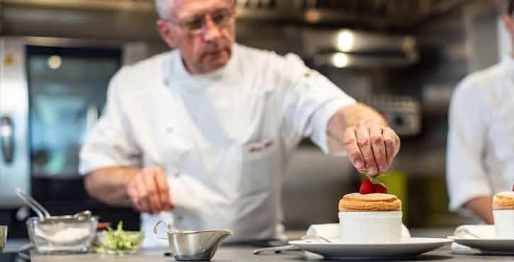 Alain Roux places a raspberry on top of a souffle he is plating at this restaurant The Waterside Inn. The iCombi Pro can be seen in the kitchen behind him.