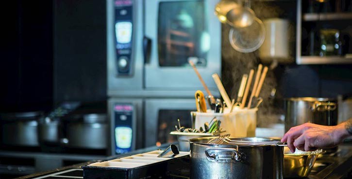 a commercial kitchen where a chef uses a stove pot with smart ovens in the background