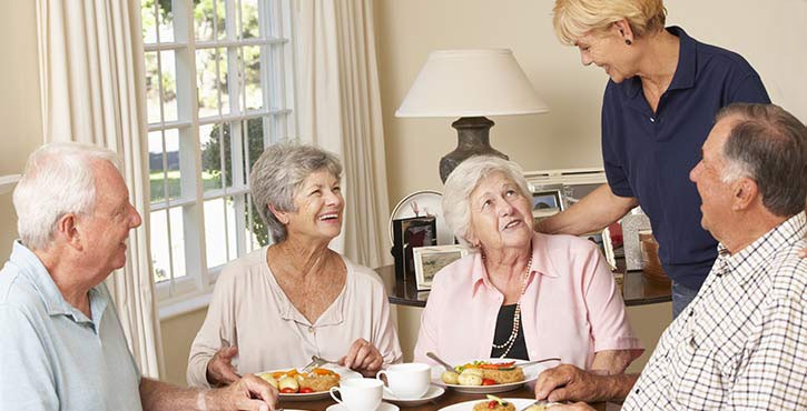 a care home worker speaks to elderly residents over a meal