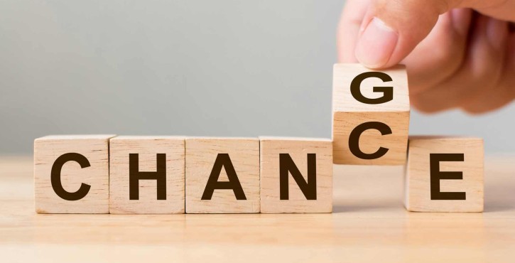 A line of wooden blocks on the table, each with a letter on them, spelling out the word chance but with the second c being turned round by a hand, to a g, to spell out change.
