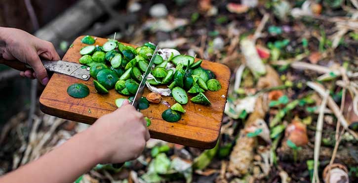 vegetables from a chefs chopping board being scraped into a compost bin