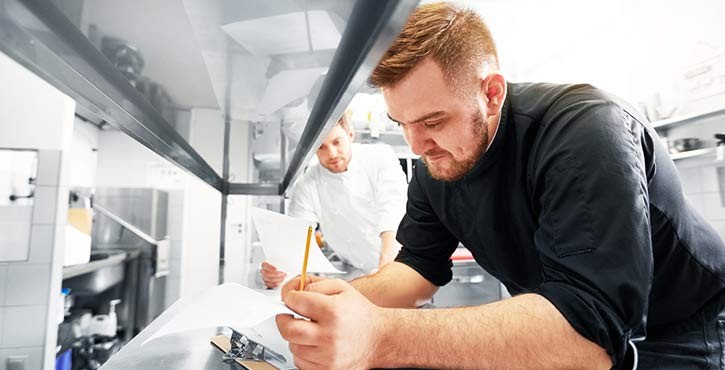 a Head chef writes down and checks his list with another chef onlooking