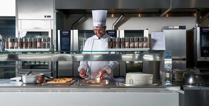 A male chef uses a temperature probe to check the temperature of the food he is serving as part of a buffet line.