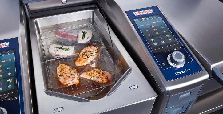 The iVario Pro advanced bratt pan is open on one side and there is 3 vaccum packed pieces of chicken and 3 vaccuum packed pieces of duck cooking in a sous-vide water bath.