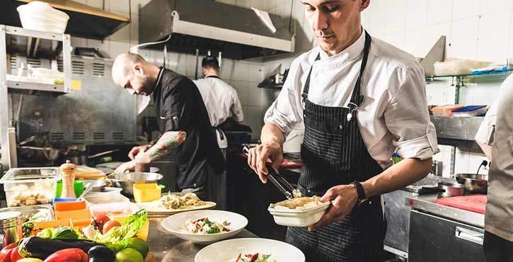 head chef completing a dish in the kitchen surrounded by other chefs working