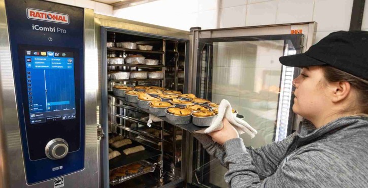 a woman loads multiple food items into a combi-steamer oven