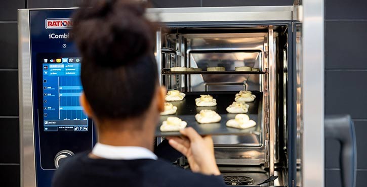 A young female chef loads a tray of frozen pastries into a RATIONAL iCombi Pro combi-steam oven