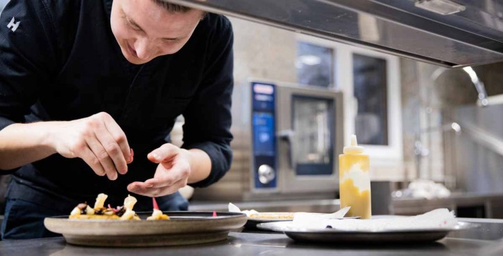 A chef finishes plating a delicious dish with a bottle of yellow sauce, the iCombi Pro can be seen in the background.