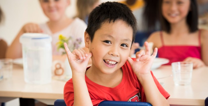 A young Asian school boy pulls a funny face at the camera as he leans over the back of his lunch chair
