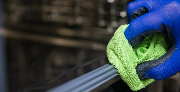 A blue gloved hand wipes down surfaces with a green cloth to keep things clean.