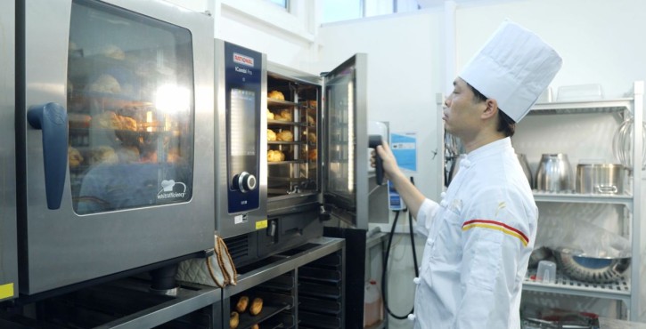Chef opening the RATIONAL iCombi Pro combi oven with freshly baked pastries inside.