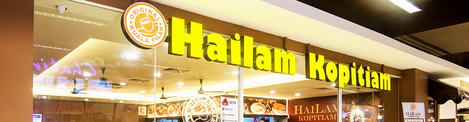 Interior of Hailam Kopitiam restaurant with customers seated at tables, under bright lighting and large signage displaying the restaurant‘s name.