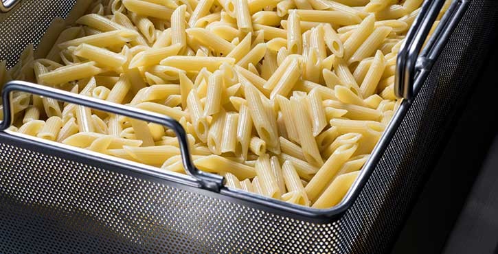 Cooked penne pasta in a metal basket.