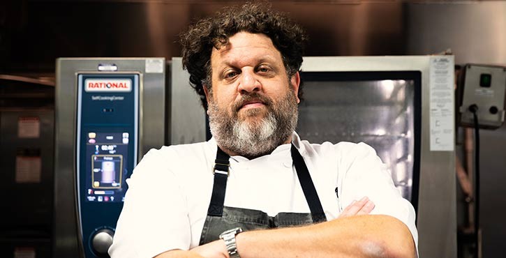Person posing confidently with arms crossed, standing in a commercial kitchen in front of a Rational SelfCookingCenter oven.