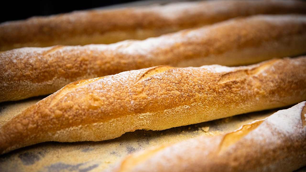 Freshly baked baguettes with a golden crust and flour dusting on a baking tray.