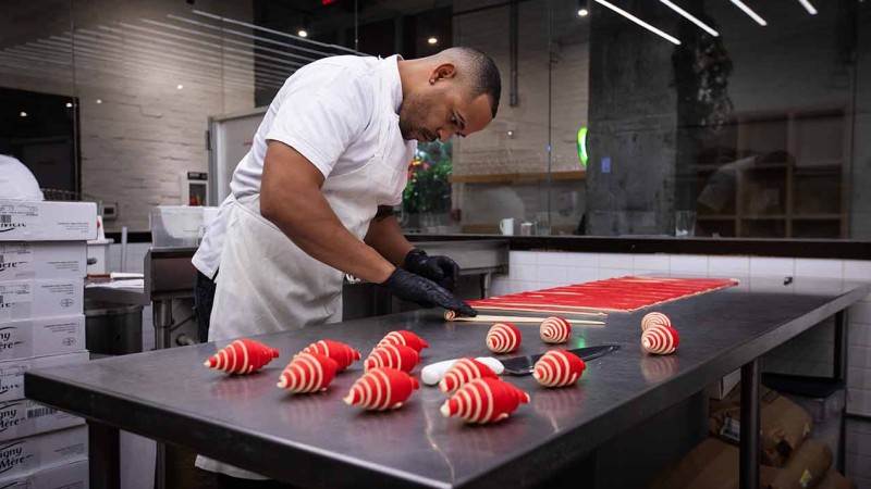 A baker meticulously arranging red and white croissants on a counter in a modern kitchen.