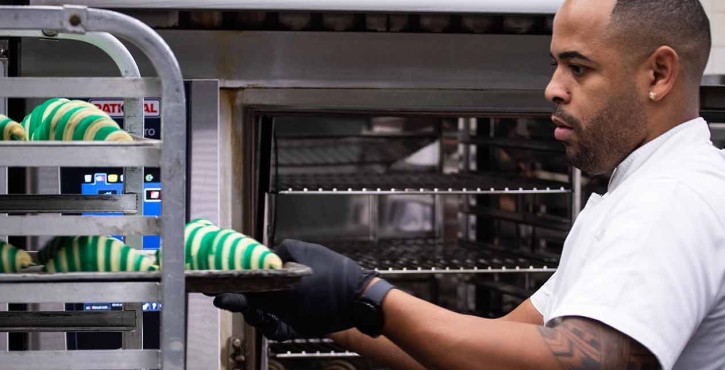 A baker placing green and white striped croissants into a Rational iCombi oven in a professional kitchen.