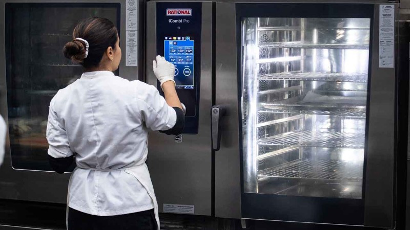 A chef operating a Rational iCombi Pro oven in a modern kitchen, with green croissants arranged on the counter.