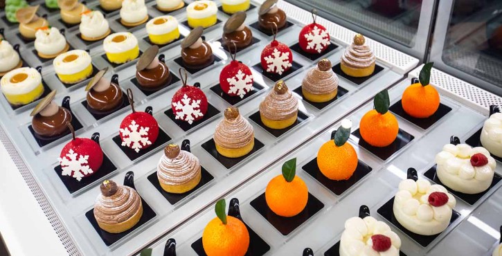 Display of assorted decorative pastries and desserts in a pastry counter, including festive-themed treats.