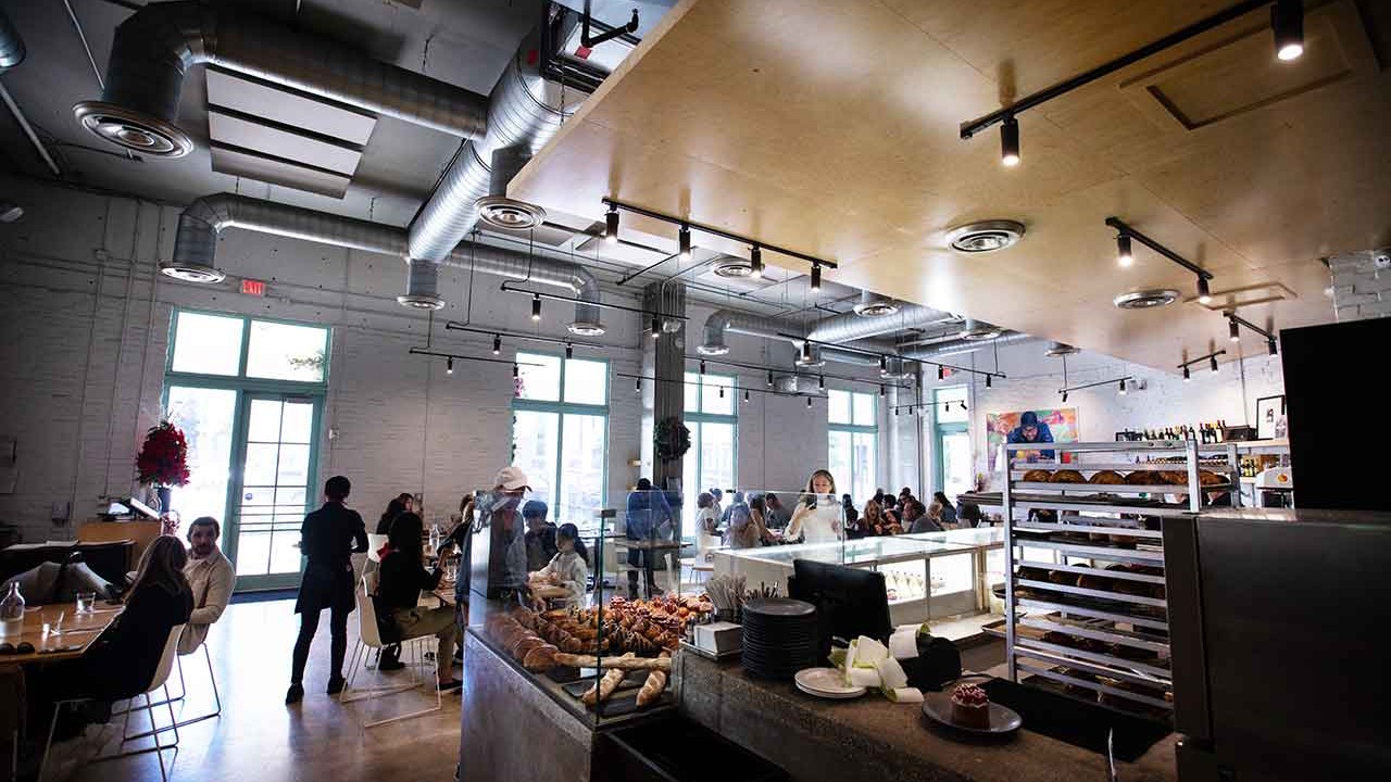 Interior view of a bustling café with customers dining and a display of baked goods in the foreground.