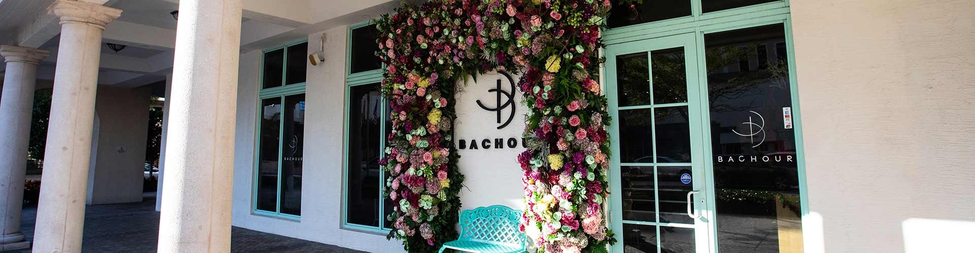 The entrance of Bachour, featuring a flower-covered wall and a turquoise bench in front of the glass doors.