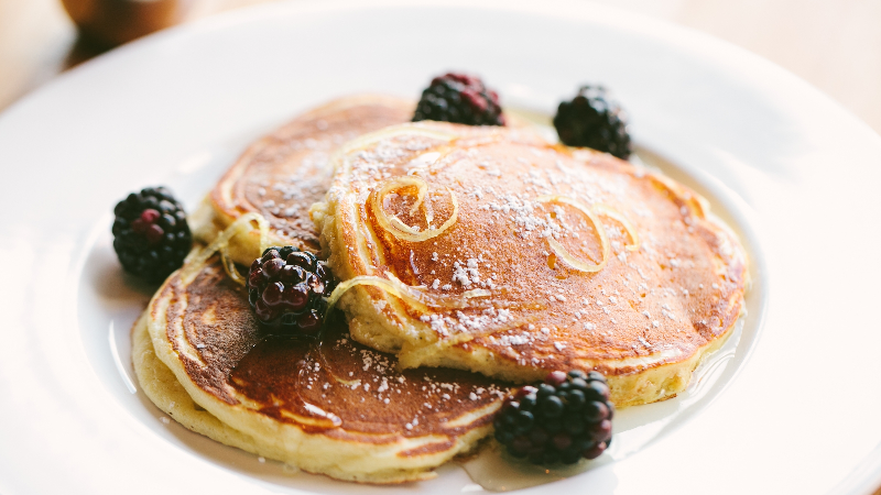 Plate of light and fluffy pancakes topped with blackberries and dusted with powdered sugar.