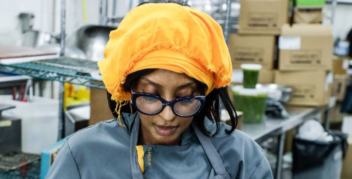 Chef in orange head covering shaping dough in a professional kitchen.