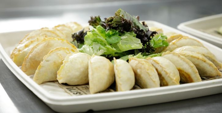 Tray of baked empanadas arranged around fresh salad in a professional kitchen.