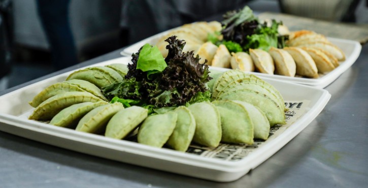 Trays of green and golden empanadas with fresh salad in a professional kitchen.