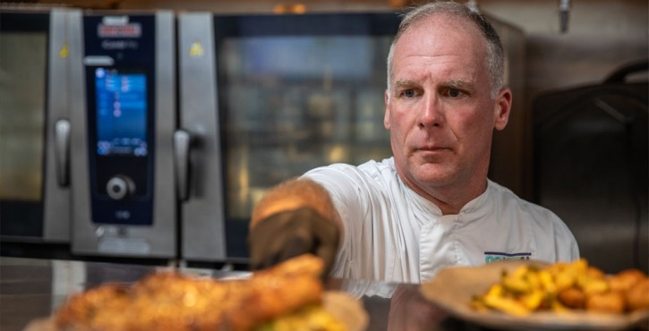 Chef plating dishes in a professional kitchen with a RATIONAL iCombi Pro combi oven in the background.