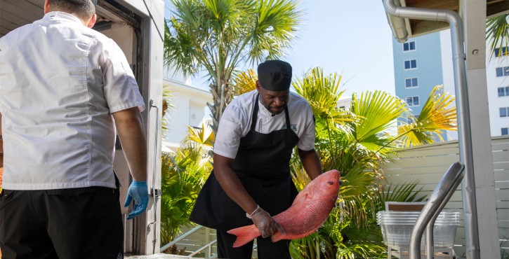 Chef unloading a fresh red snapper from a delivery truck outside Coastal Orange Beach restaurant.