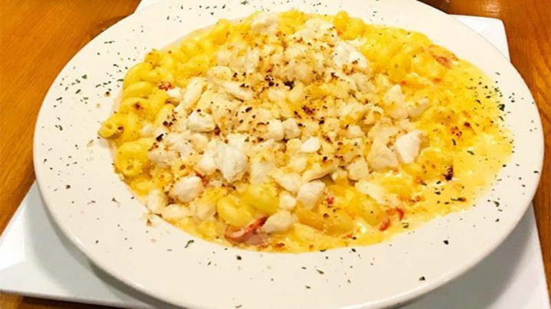 A creamy pasta dish with cavatappi, topped with chunks of crab meat and a sprinkle of black pepper on a white plate.