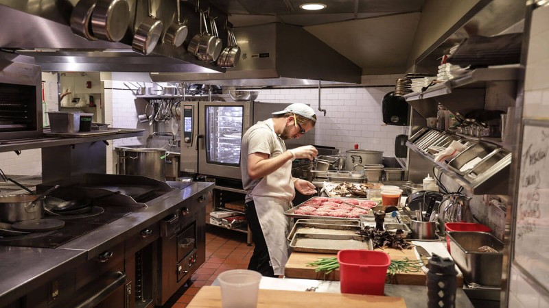 A chef in a busy kitchen preparing food with various ingredients and equipment around.