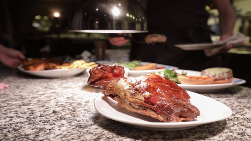 A roasted piece of meat on a plate with side dishes in the background at a restaurant.