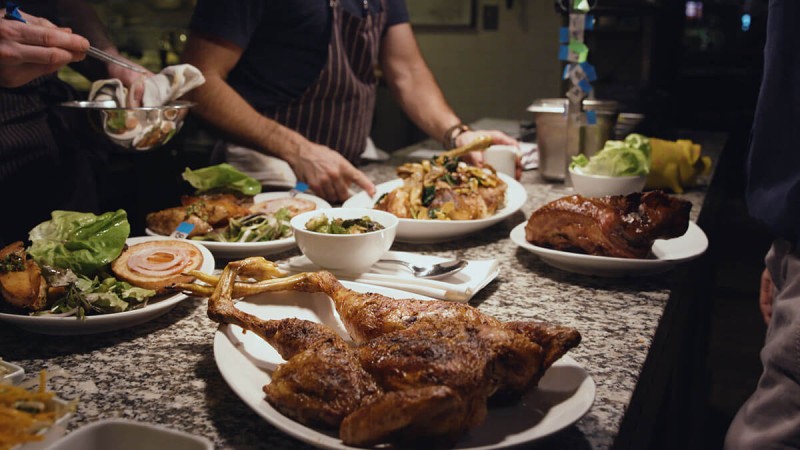 A chef preparing a variety of dishes including roasted chicken and sides on a kitchen counter.