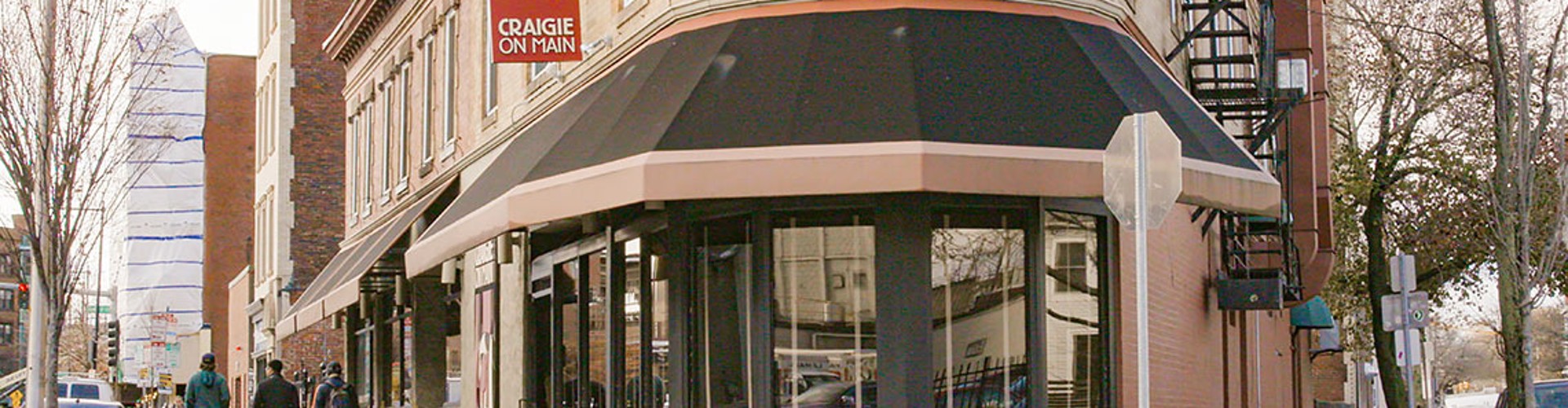 The exterior view of Craigie on Main restaurant with people walking by and trees in the foreground.