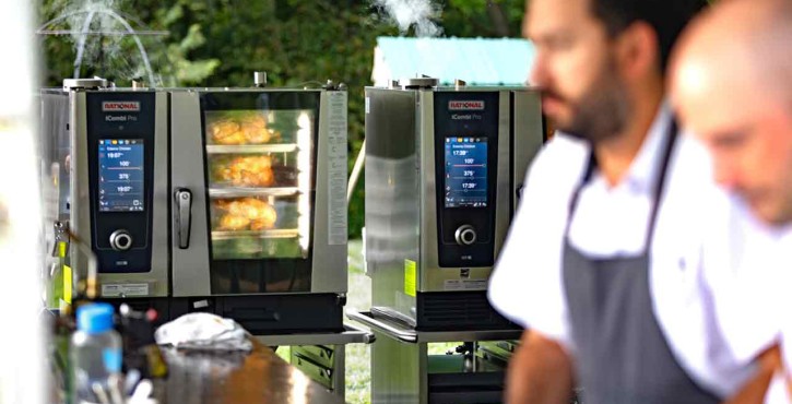 Two chefs work in a kitchen outdoors with Rational iCombi Pro ovens steaming food in the background.