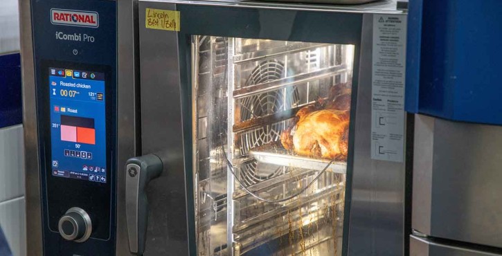 A close-up of a Rational iCombi Pro oven displaying roasted chicken inside, with a digital timer showing cooking details.