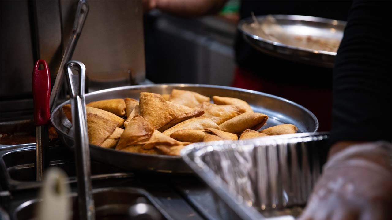 A tray filled with golden-brown pastries, with tongs resting beside it and a hand in the background preparing food.