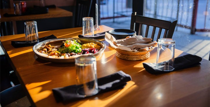 A beautifully set dining table with a large platter of colorful food, glasses, and a stack of napkins in a restaurant.