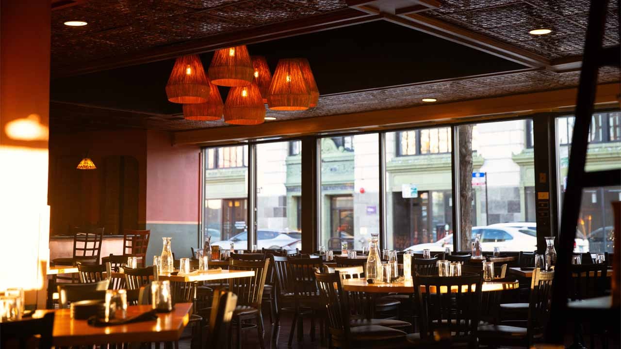 Interior view of Demera Ethiopian Restaurant featuring wooden tables, chairs, and pendant lights with large windows showing the street outside.