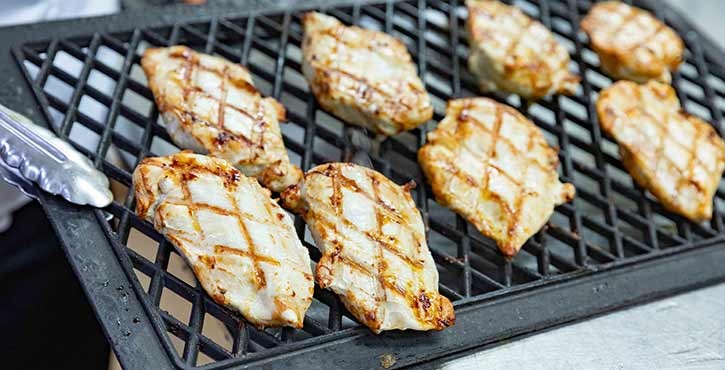 Grilled chicken fillets with char marks on a grill rack, showcasing a deliciously cooked meal.