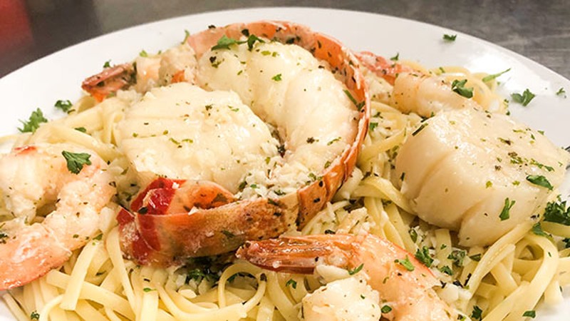 Plate of seafood pasta featuring shrimp, lobster, and scallops garnished with parsley.
