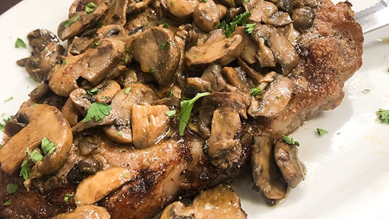 Plate of steak topped with sautéed mushrooms and garnished with parsley.