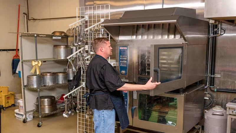 A chef in a black shirt operating a Rational cooking unit in a professional kitchen with various equipment.