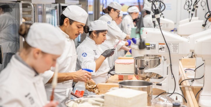 Culinary students decorating cakes and pastries in a professional training kitchen.