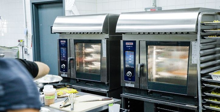Two RATIONAL iCombi Pro combi ovens in a commercial kitchen beside a chef at a prep table.