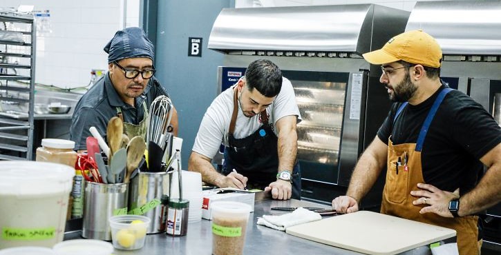 Three chefs reviewing notes at a prep table in front of RATIONAL iCombi Pro combi ovens.
